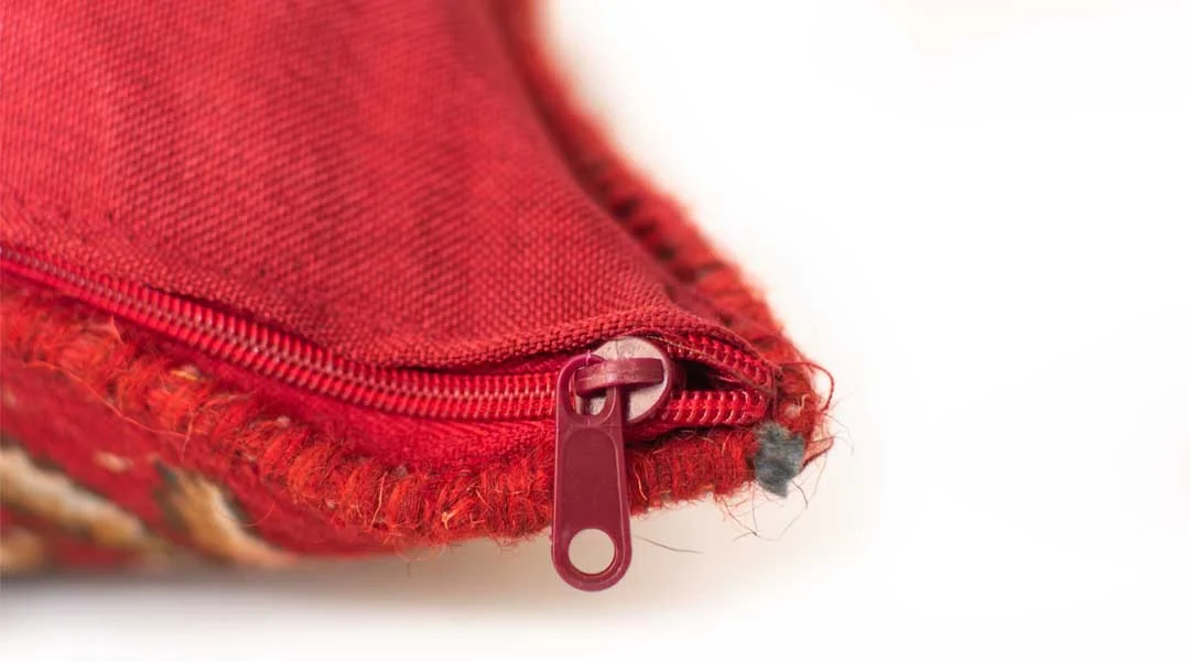 Close-up side view of an authentic Persian handwoven rug cushion showing the premium red fabric backing, neat stitching, and high-quality hidden zipper detail.