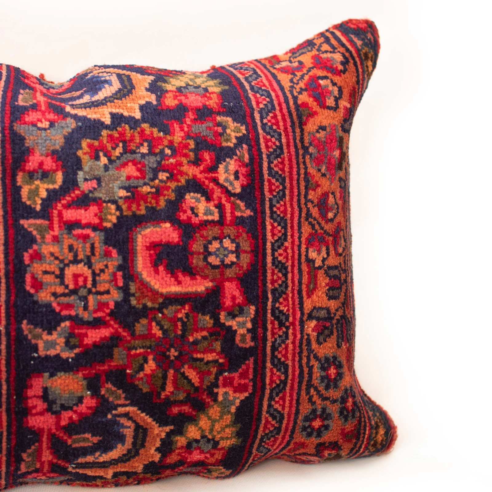 Close-up of a vintage handwoven Persian rug cushion cover with intricate red, navy, orange, and cream geometric motifs and visible wool texture.